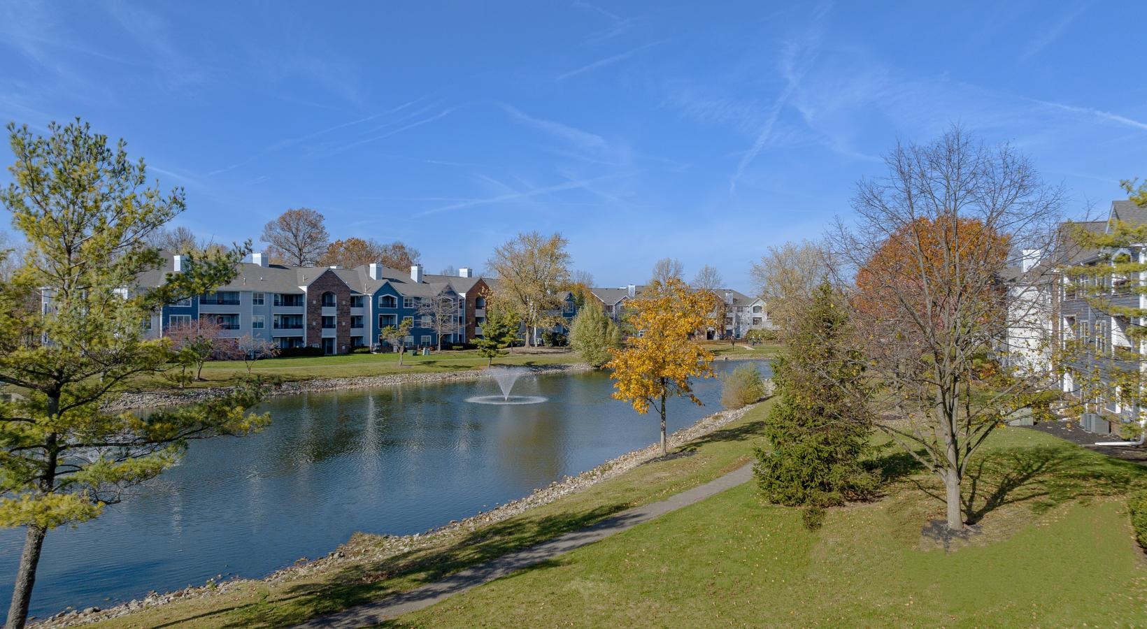 The essence of exceptional living a pond with grass and trees by it and buildings in the background